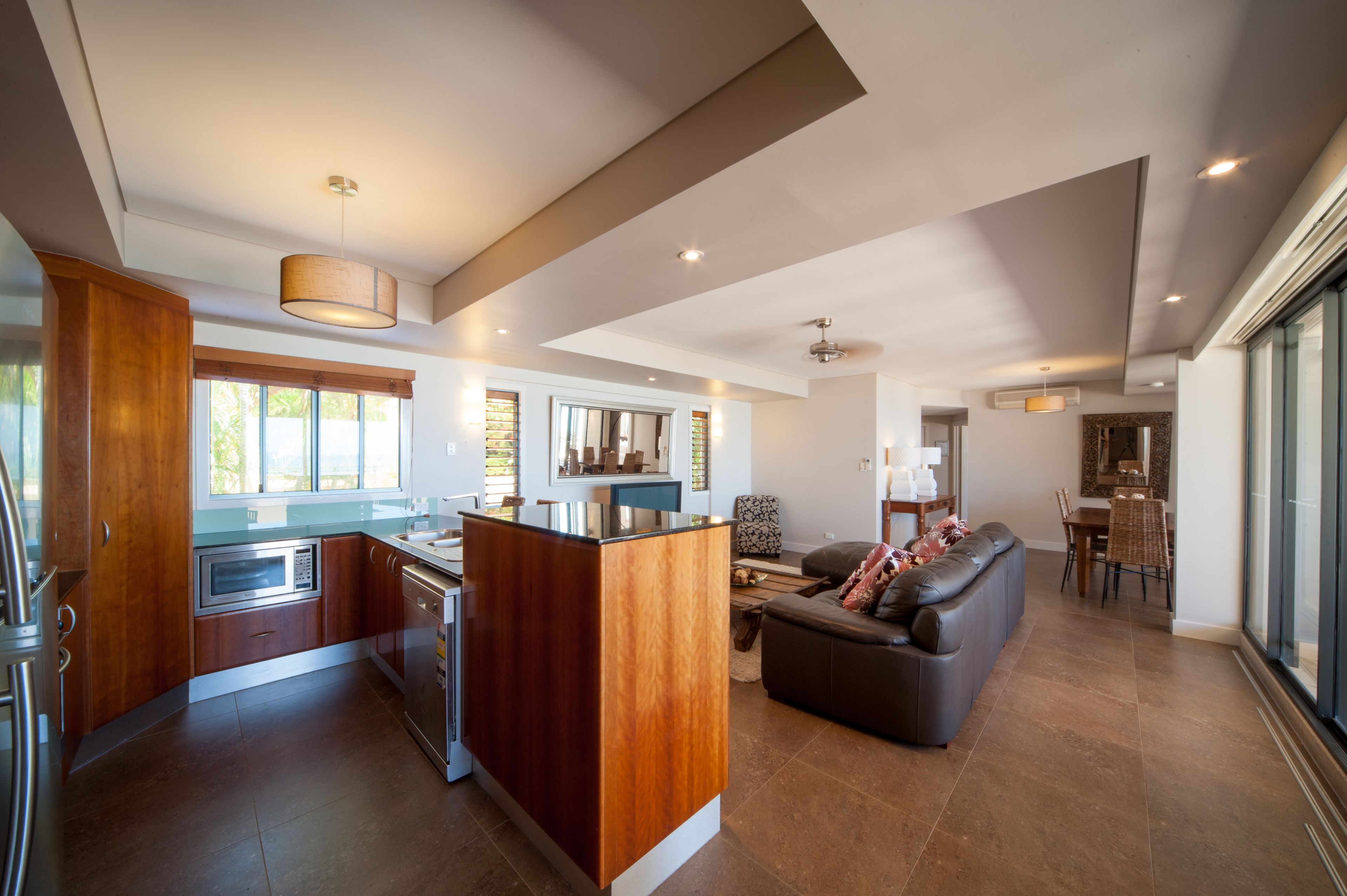 A modern kitchen with wooden cabinets, a central island, and a dining area with a sofa and table.