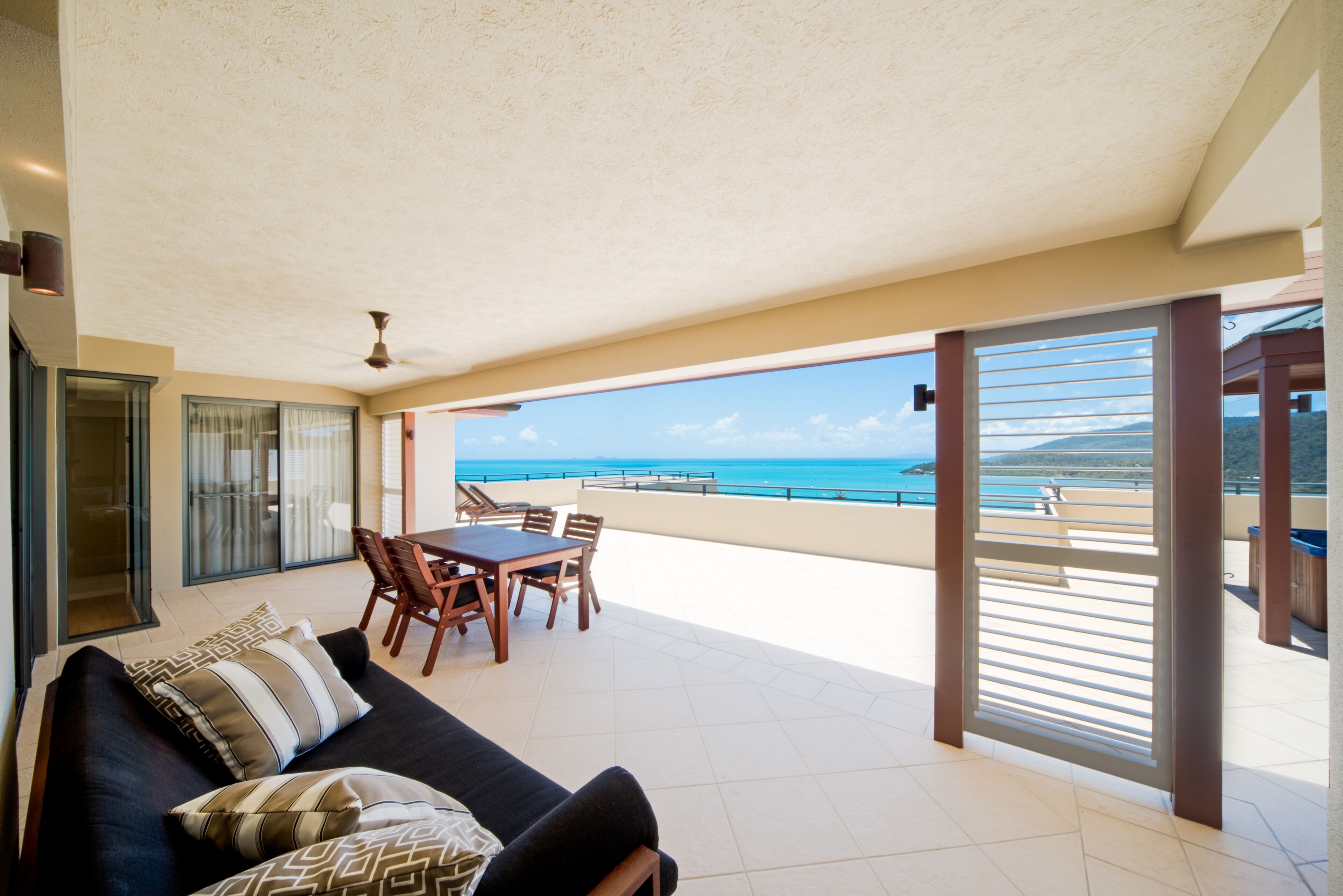 A balcony with a dining set and a sofa, overlooking a coastal view.