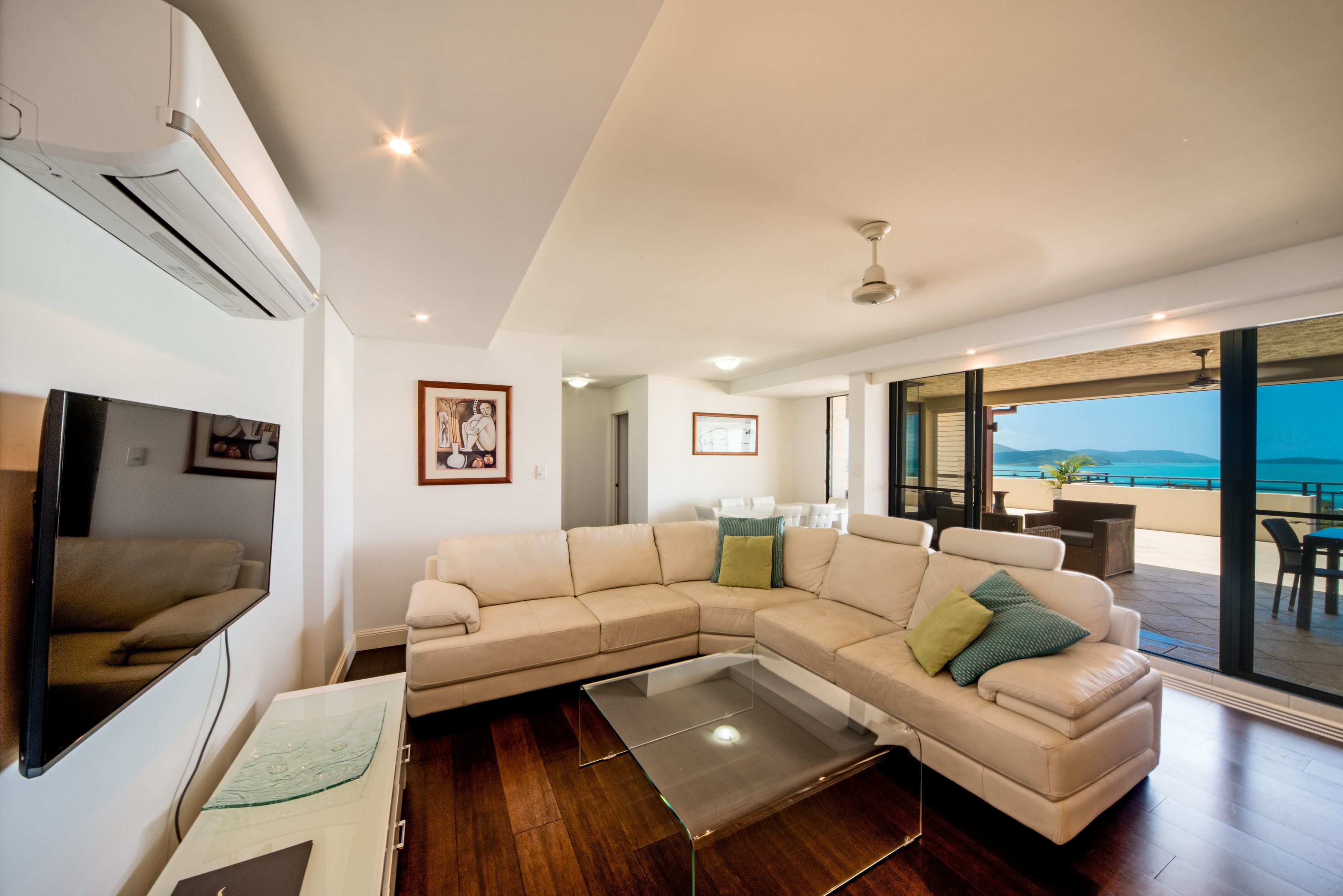 A modern living room with a sectional sofa, a glass coffee table, and a large window offering a view of the sea.