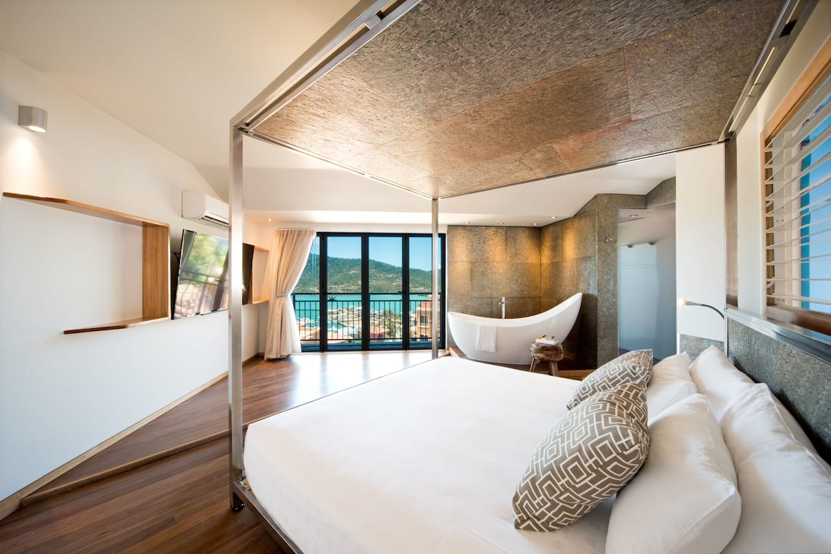 Una habitación de hotel moderna con una cama grande, una bañera y un balcón con vistas al mar.