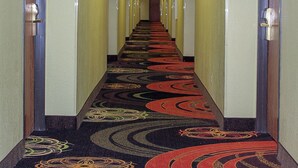 Un pasillo de hotel con pisos alfombrados, puertas a ambos lados y letreros iluminados que muestran los números de las habitaciones.
