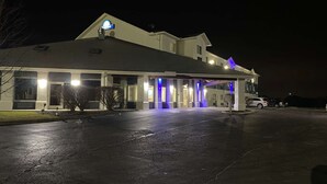 Un hotel con una entrada bien iluminada, un área exterior cubierta y un estacionamiento.