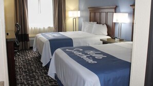 Habitación de hotel con dos camas, un ventanal con cortinas, una lámpara de pie y una alfombra estampada.