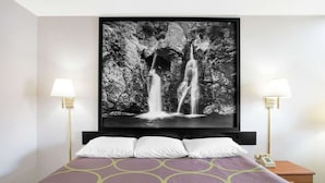 A hotel room with a bed, two bedside lamps, a nightstand with a phone, and a large black and white waterfall painting on the wall. - Super 8 by Wyndham Christiansburg (Christiansburg)
