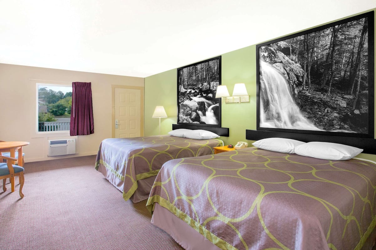 Une chambre d’hôtel avec deux lits, un bureau, une fenêtre avec des rideaux et un grand tableau représentant une cascade au mur.