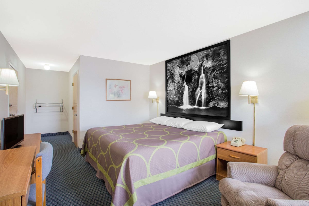 Une chambre d’hôtel équipée d’un lit, d’un bureau, d’une chaise, d’une table de chevet avec un téléphone et d’un téléviseur fixé au mur.