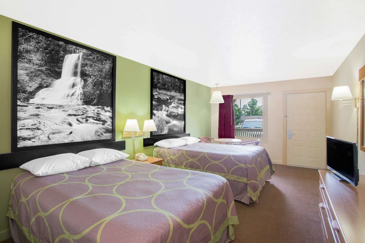 Une chambre d’hôtel avec deux lits, une télévision, un bureau et deux grandes images de cascades accrochées au mur.