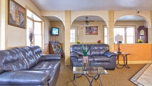 A living room with two leather sofas, a glass coffee table, and a television on the wall. - Super 8 by Wyndham Christiansburg (Christiansburg)