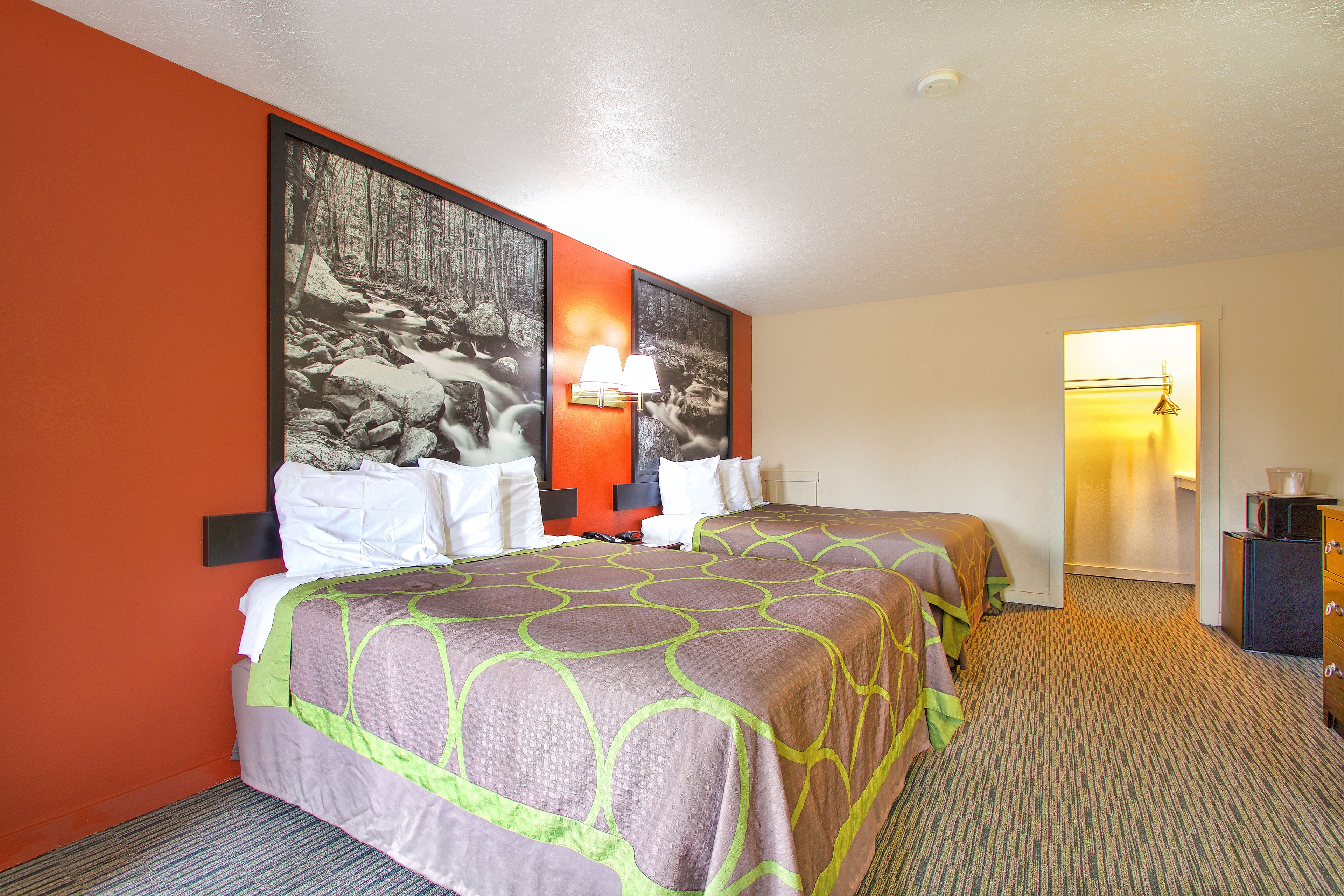 A hotel room with two beds, a large framed picture on the wall, a lamp, and a small desk.