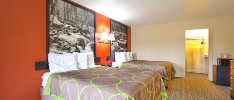 A hotel room with two beds, a large framed picture on the wall, a lamp, and a small desk.