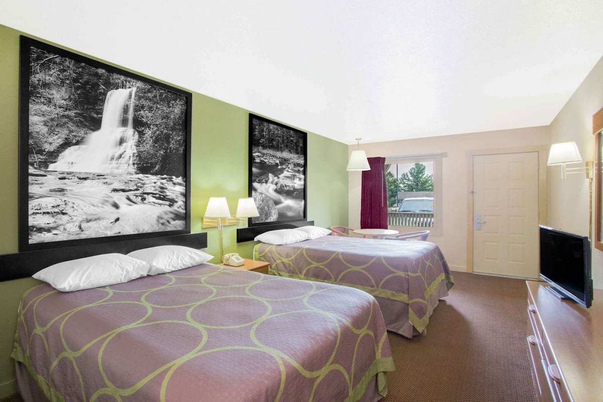 Une chambre d’hôtel avec deux lits, une télévision, un bureau et une grande peinture représentant une cascade au mur.