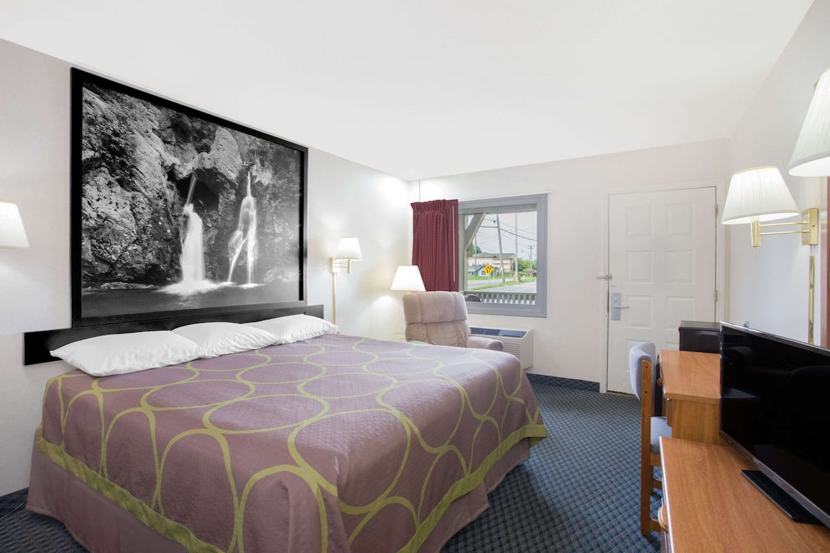 Une chambre d’hôtel avec un grand lit, un téléviseur à écran plat, un bureau et une fenêtre avec des rideaux.