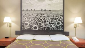 Een hotelkamer met een groot schilderij van een zonnebloem aan de muur, een bed met drie kussens en twee nachtkastjes met lampen en telefoons.