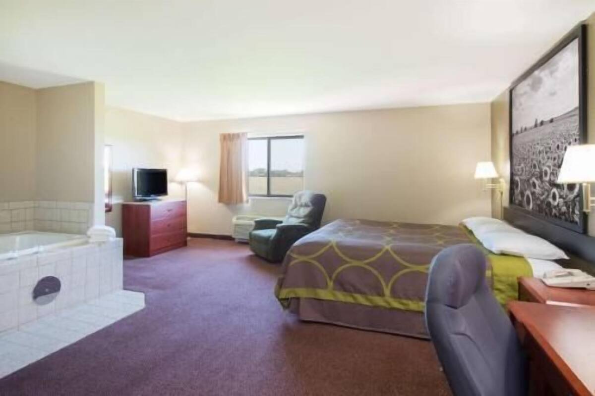 Une chambre d’hôtel comprenant un lit, une chaise, un bureau, une télévision, une fenêtre et une salle de bain avec une baignoire.