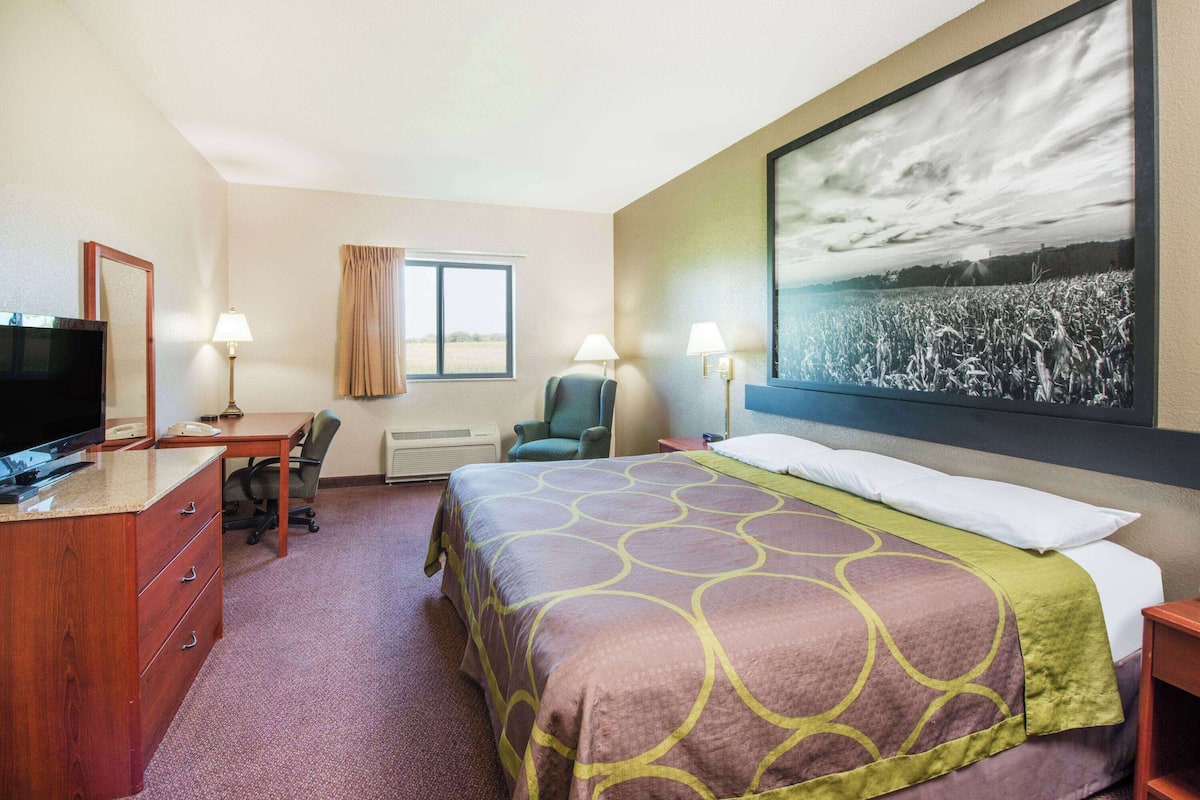Une chambre d’hôtel équipée d’un lit, d’un bureau, d’une chaise, d’une télévision et d’une grande fenêtre.
