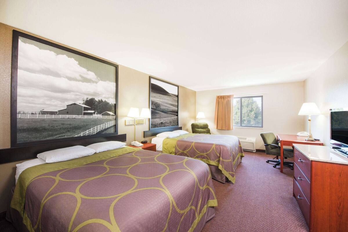 Une chambre d’hôtel avec deux lits, un bureau, une chaise et un téléviseur.