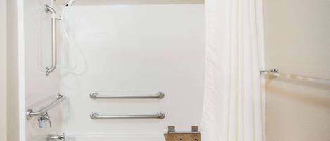 Une baignoire équipée de barres d’appui, d’un flexible de douche et d’une étagère en bois.