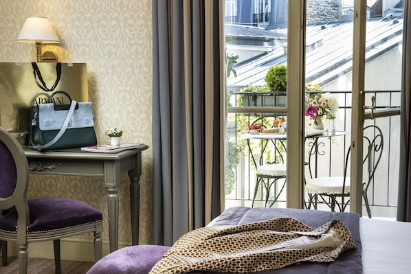 A hotel room with a bed, a chair, a desk with a lamp, a handbag, and a view of the outside balcony. - Hotel Arioso (Paris)