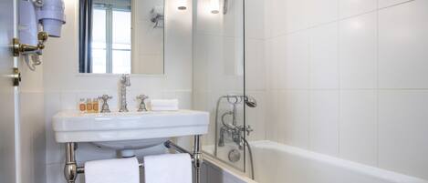 Un baño moderno con un lavamanos, espejo y bañera blancos. Dos toallas cuelgan del perchero.