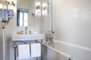 A modern bathroom with a white sink, mirror, and bathtub. There are two towels hanging on the towel rack. - Hotel Arioso (Paris)