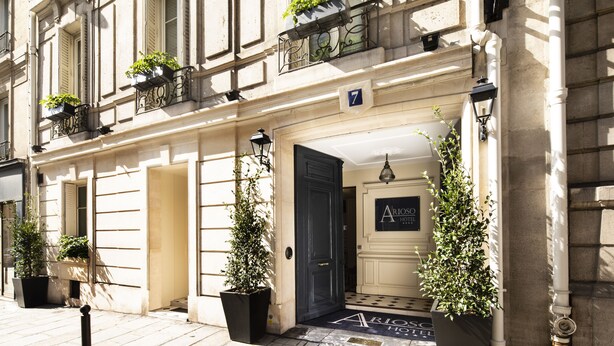 Entrada de hotel con una puerta azul oscuro, plantas en macetas y un letrero que dice "ARIOS HOTEL".