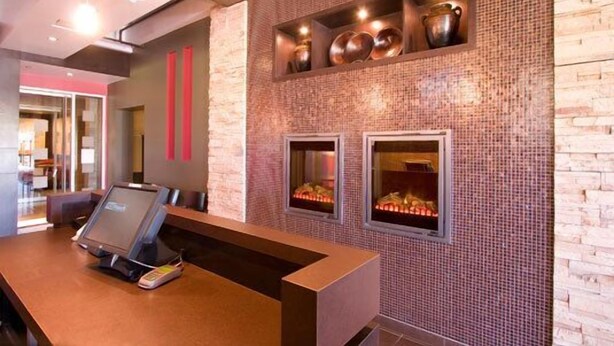 A reception area with a modern design, featuring a reception desk, a fireplace, and decorative metal pots on the wall. - Woodlands Inn & Suites (Fort Nelson)
