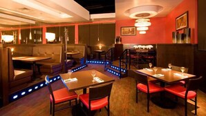 A restaurant with booths and tables, wooden flooring, and a red accent wall. - Woodlands Inn & Suites (Fort Nelson)