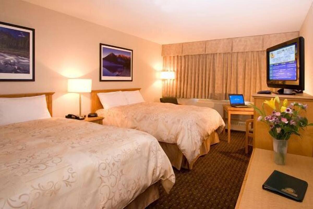 A hotel room with two beds, a desk with a computer, a TV, and a vase with flowers.