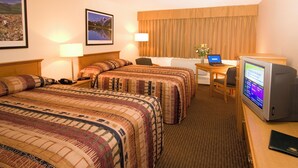 A hotel room with two beds, a desk with a laptop, a television, and framed pictures on the wall. - Woodlands Inn & Suites (Fort Nelson)