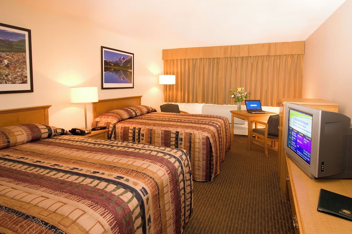 A hotel room with two beds, a desk with a laptop, a television, and framed pictures on the wall.