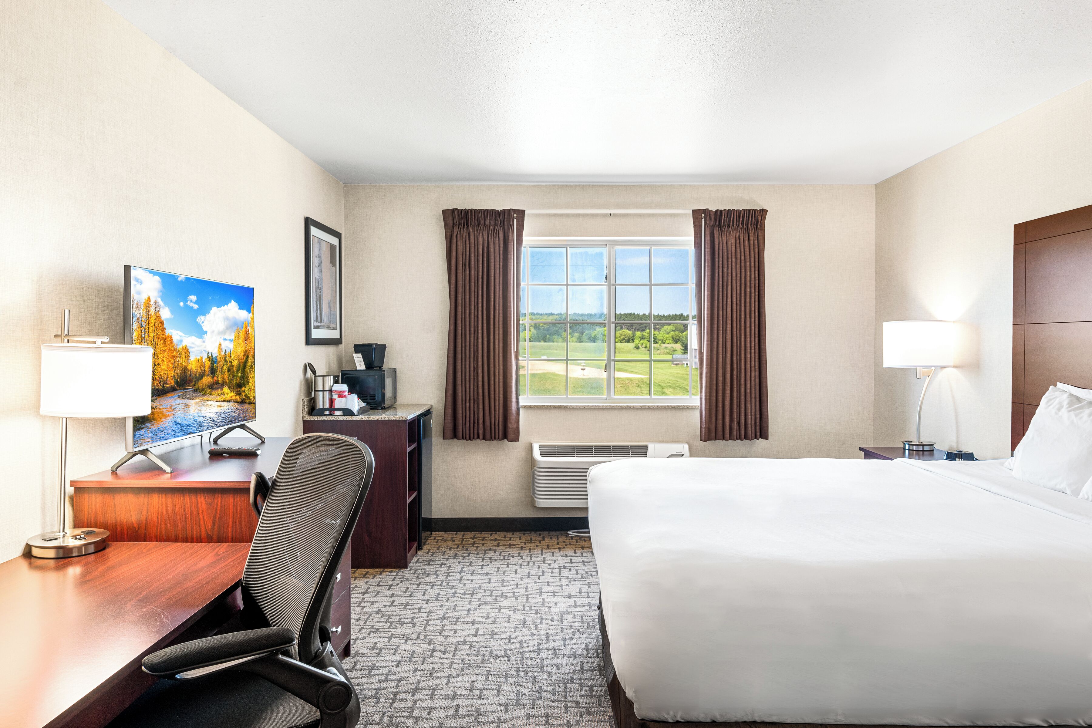 A hotel room with a bed, desk, chair, TV, and a window with curtains.