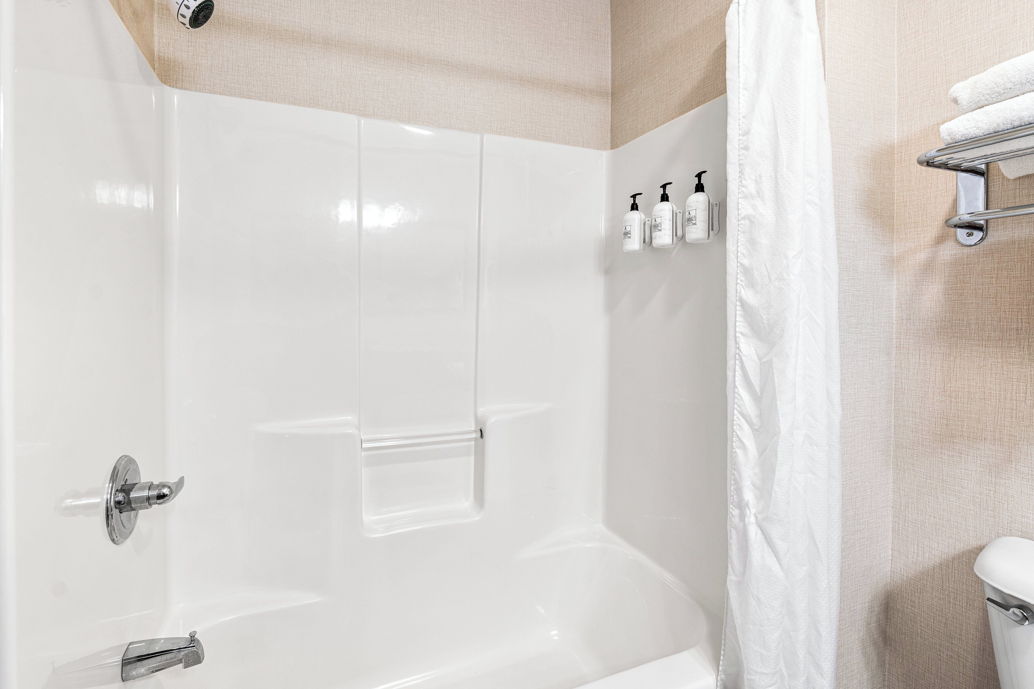 A modern bathroom with a white bathtub, a shower curtain, and toiletries on a shelf.
