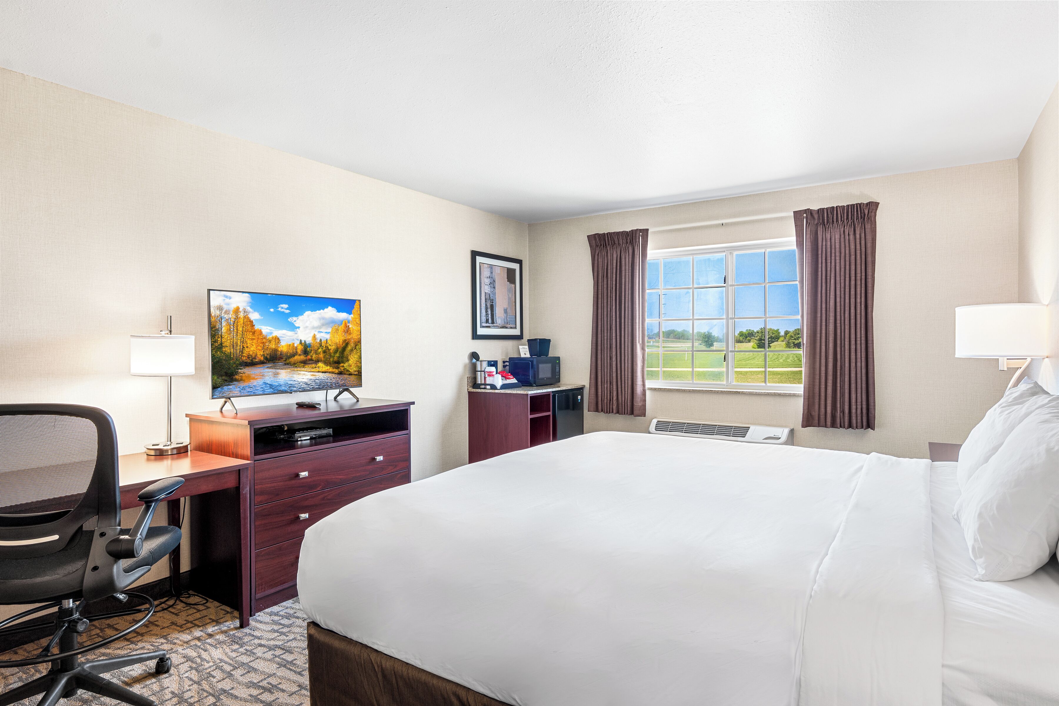 A hotel room with a bed, desk, chair, TV, and a window with curtains.