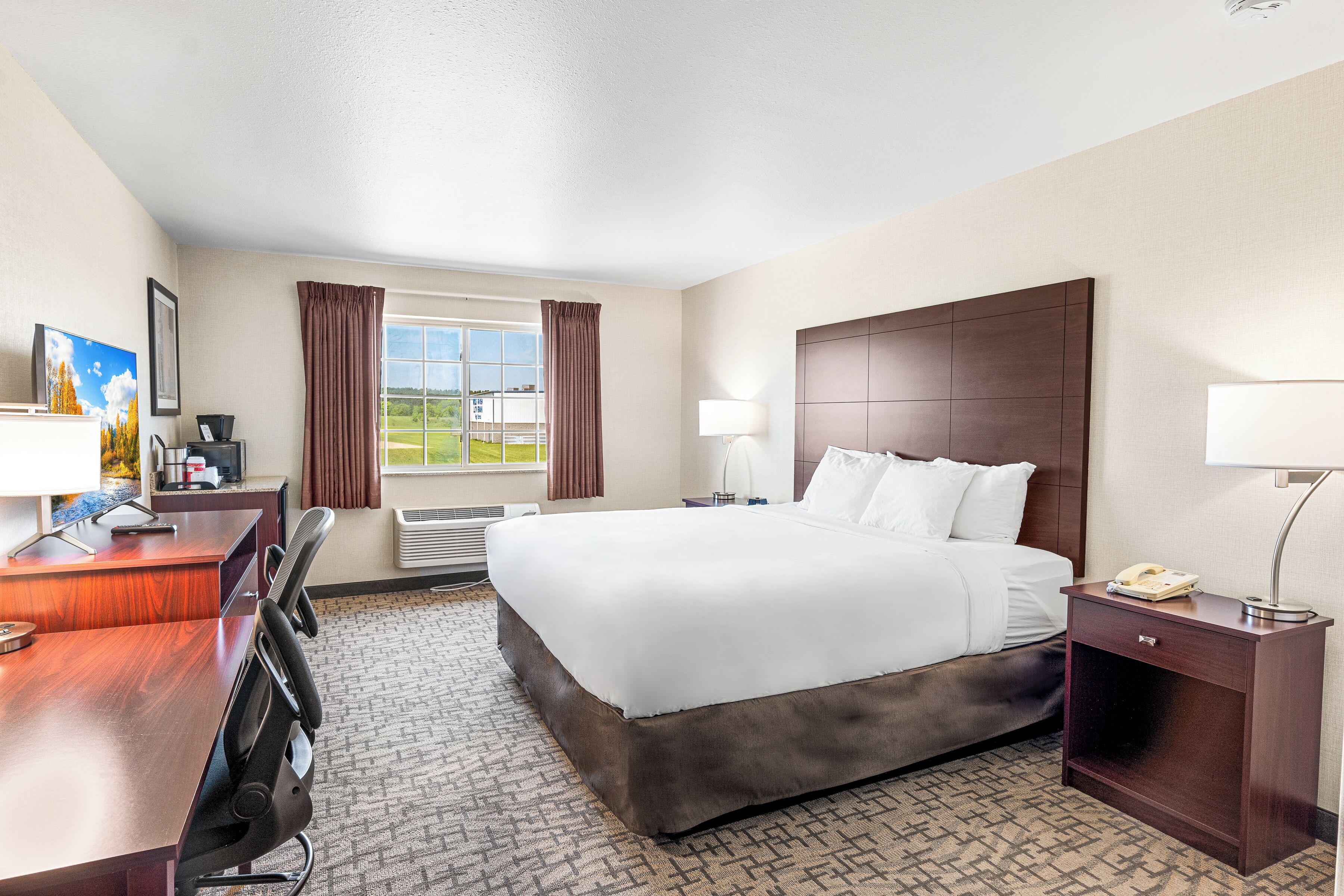 A hotel room with a large bed, a desk with a chair, a lamp, and a view of the outdoors.