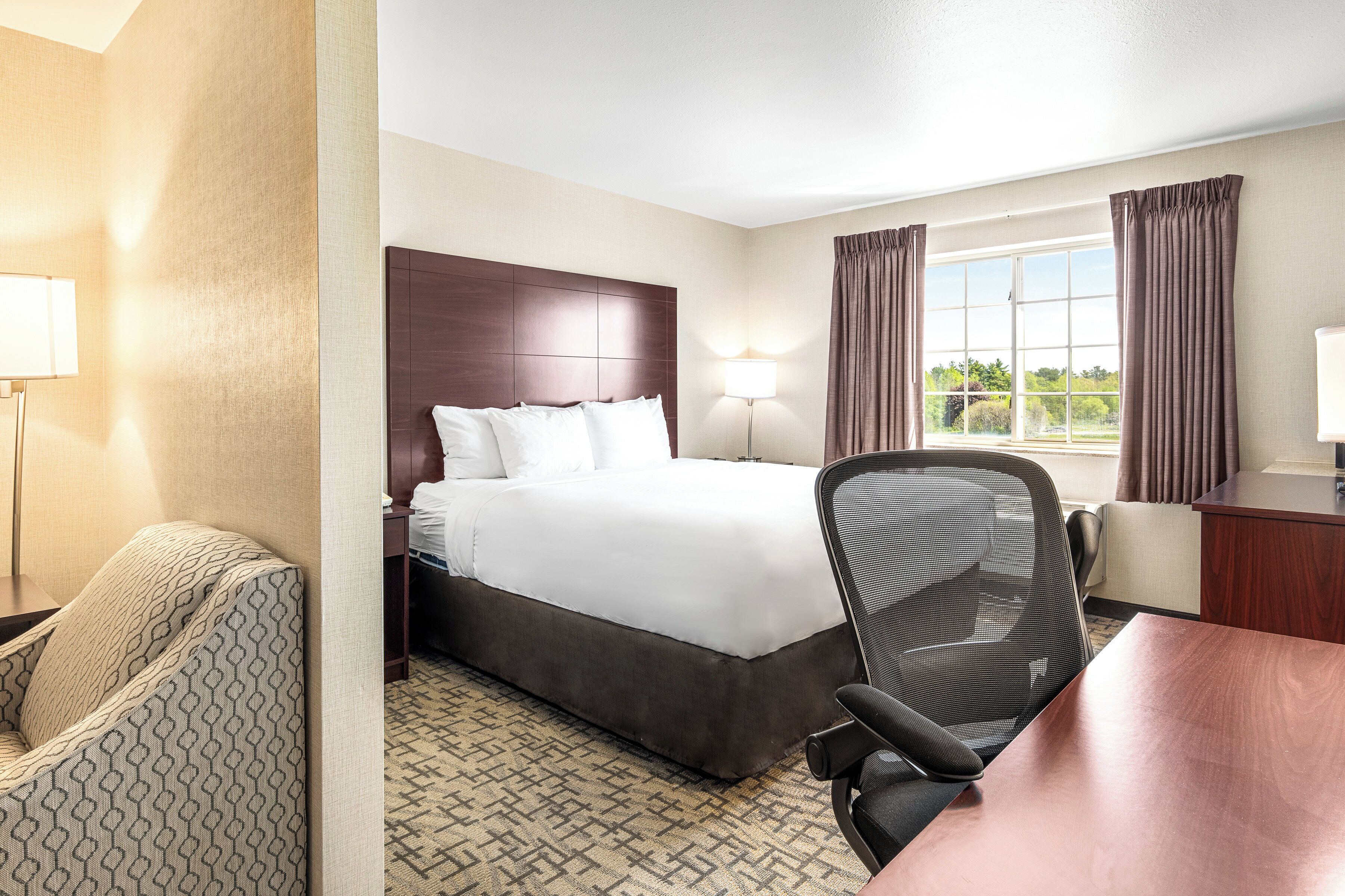 Een hotelkamer met een groot bed, een bureau, een stoel en een raam met gordijnen.