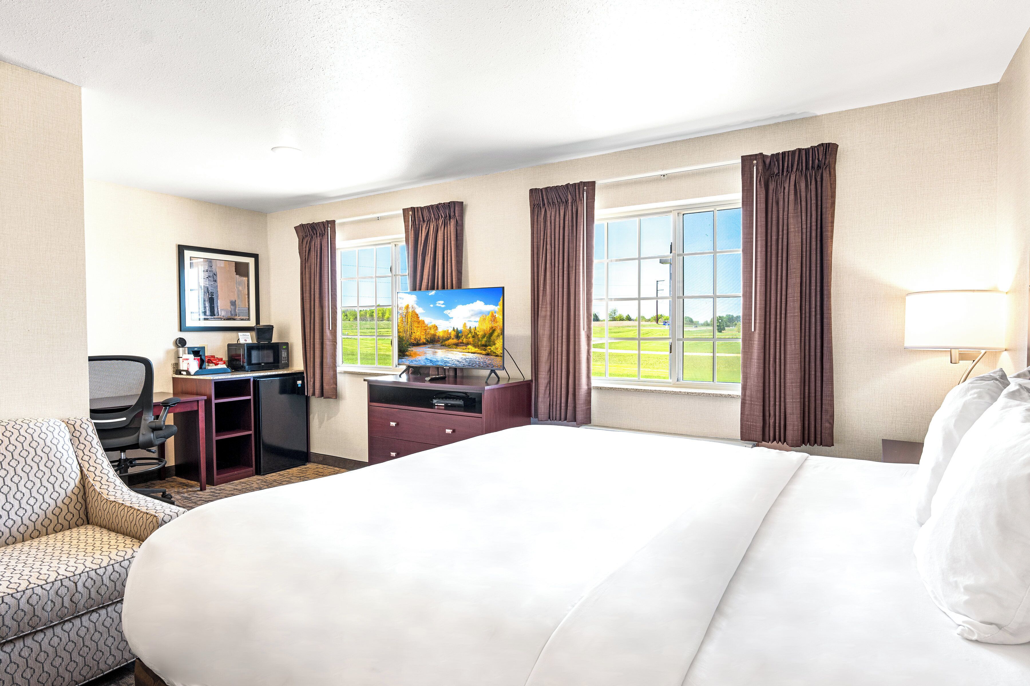 Habitación de hotel con cama, escritorio con computadora y televisor, una silla y ventana con cortinas.