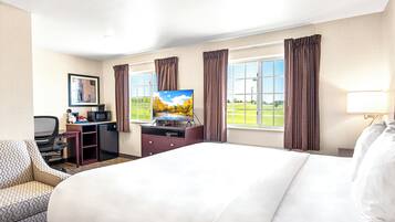 Habitación de hotel con cama, escritorio con computadora y televisor, una silla y ventana con cortinas.