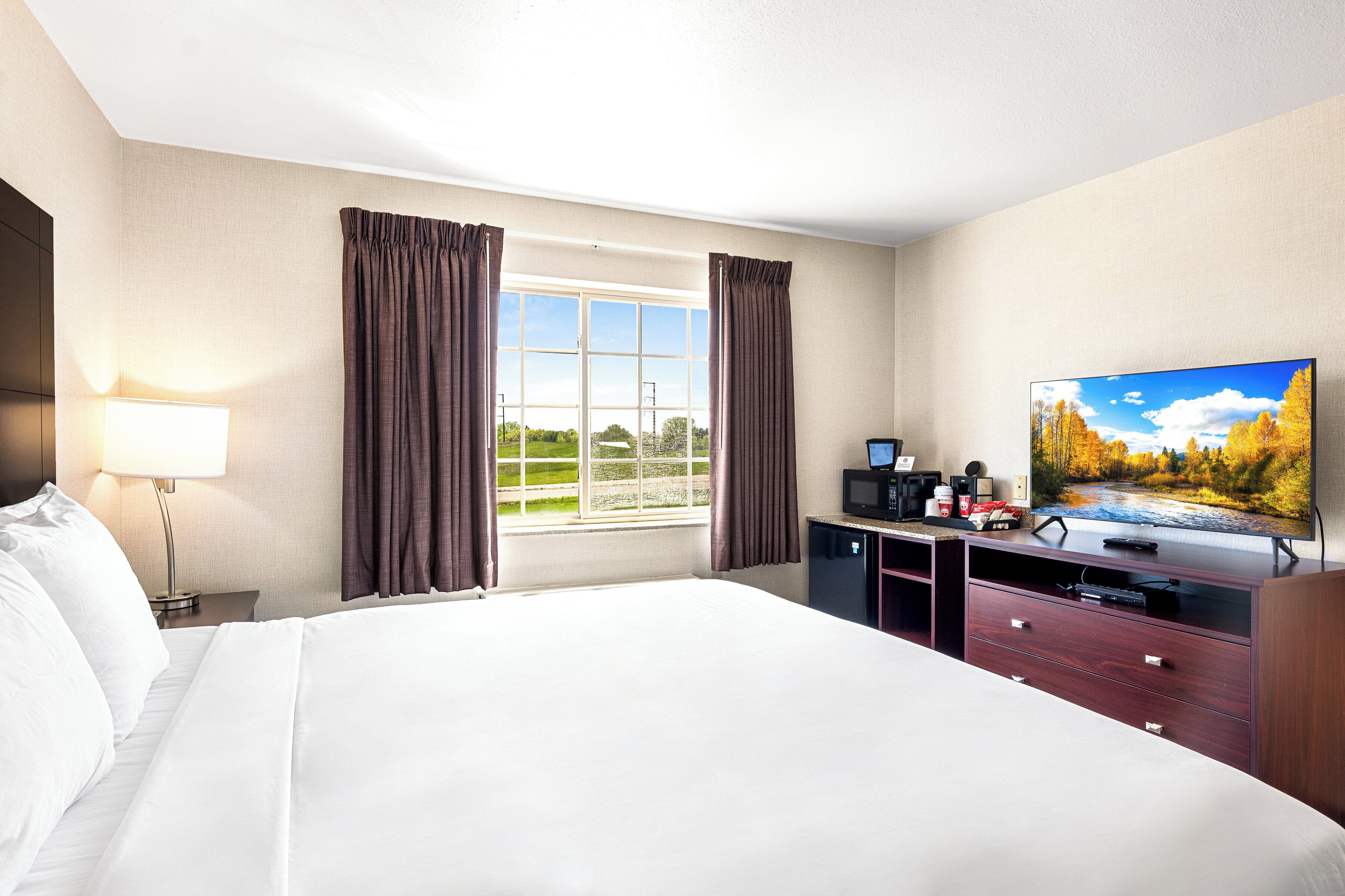 A hotel room with a large bed, a flat-screen TV, a desk with a computer, and a window with curtains.