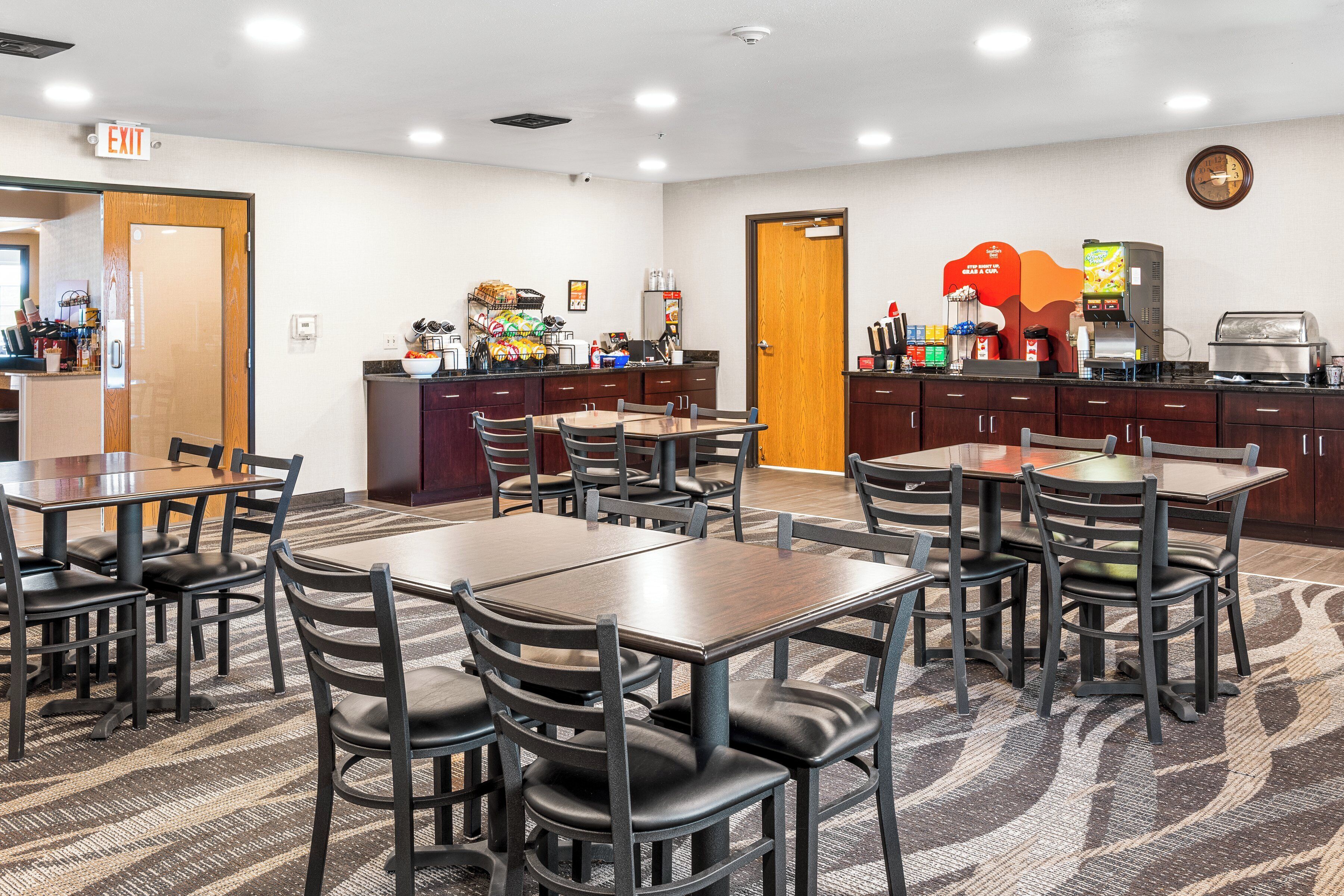 A hotel dining area with multiple tables and chairs, a coffee machine, and a clock on the wall.