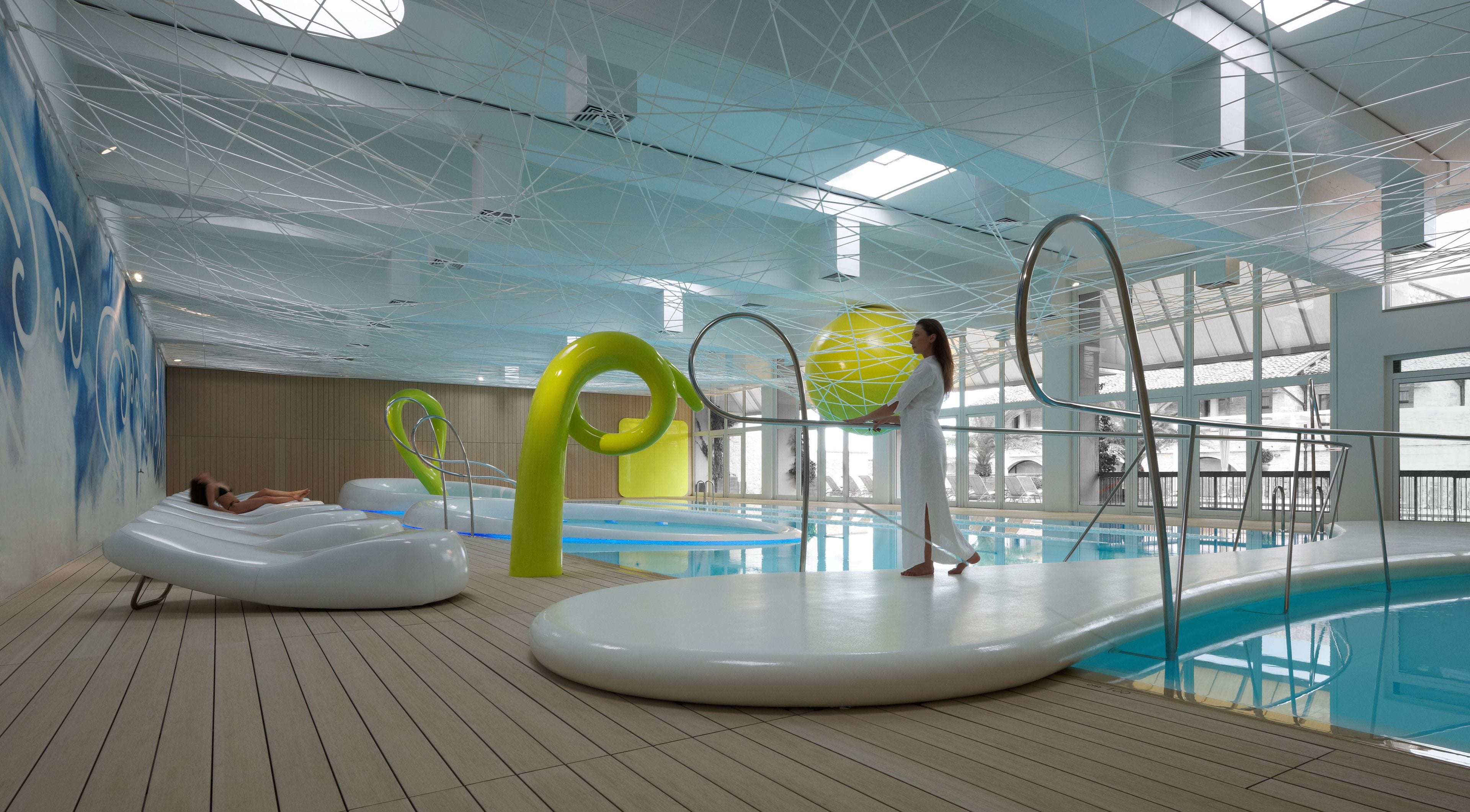 An indoor swimming pool with clear water, a wooden deck, and a modern ceiling design.