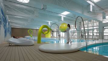 An indoor swimming pool with clear water, a wooden deck, and a modern ceiling design.