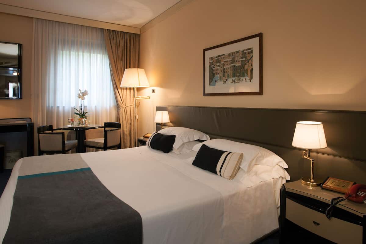 A hotel room with a large bed, bedside lamps, a desk with a telephone, and a framed picture on the wall.