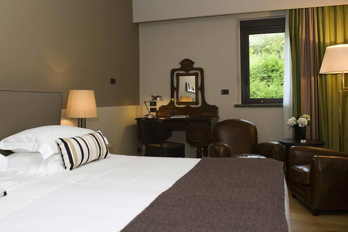 A hotel room with a bed, a desk, a chair, a lamp, and a window with curtains.