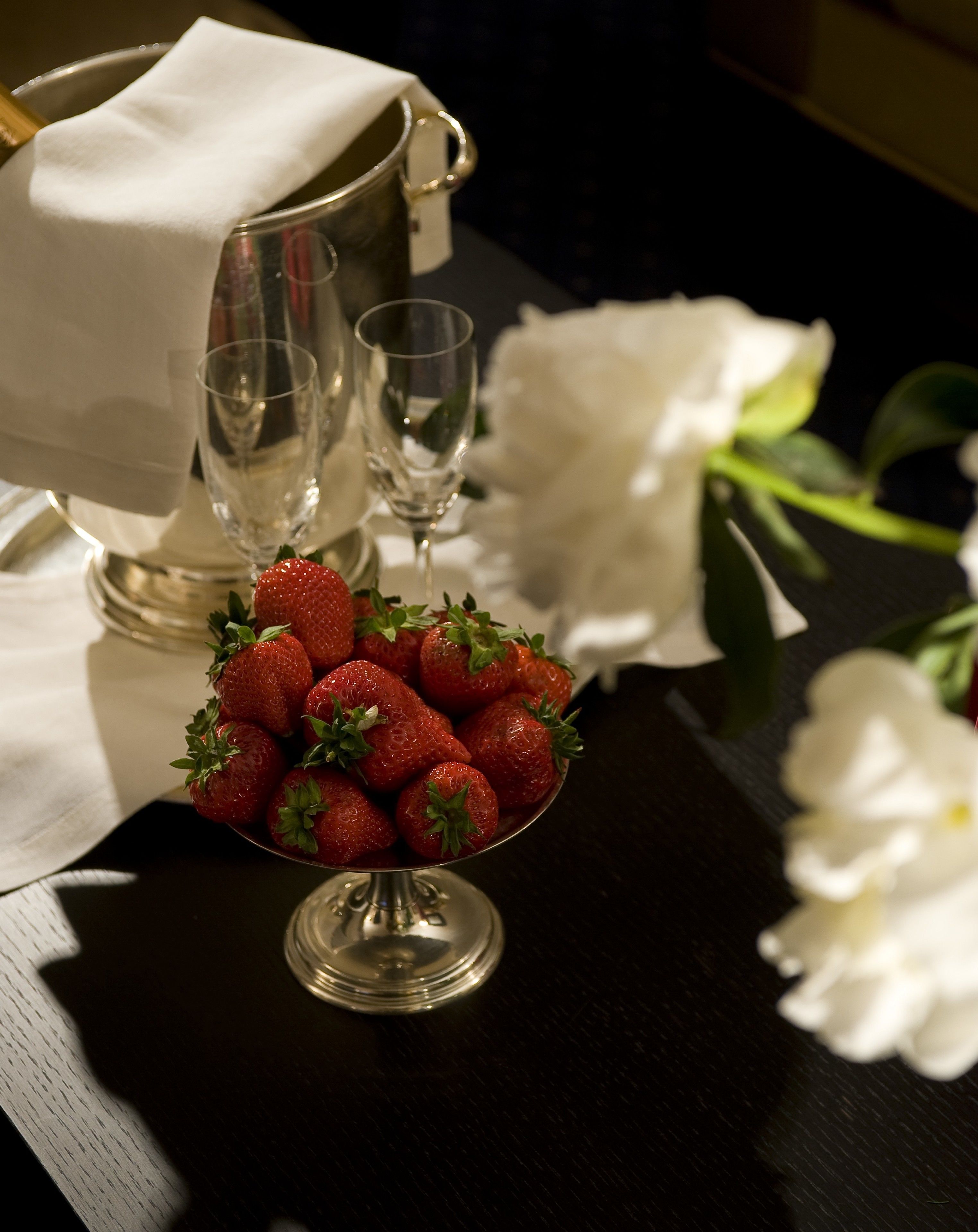 A table with a bowl of strawberries, a wine glass, and a pitcher.