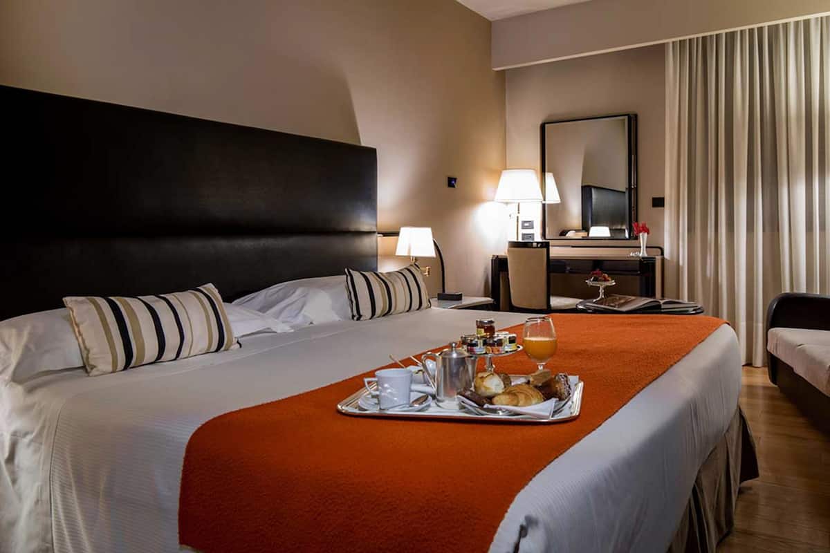 A hotel room with a large bed, a desk with a lamp, and a breakfast tray on the bed.