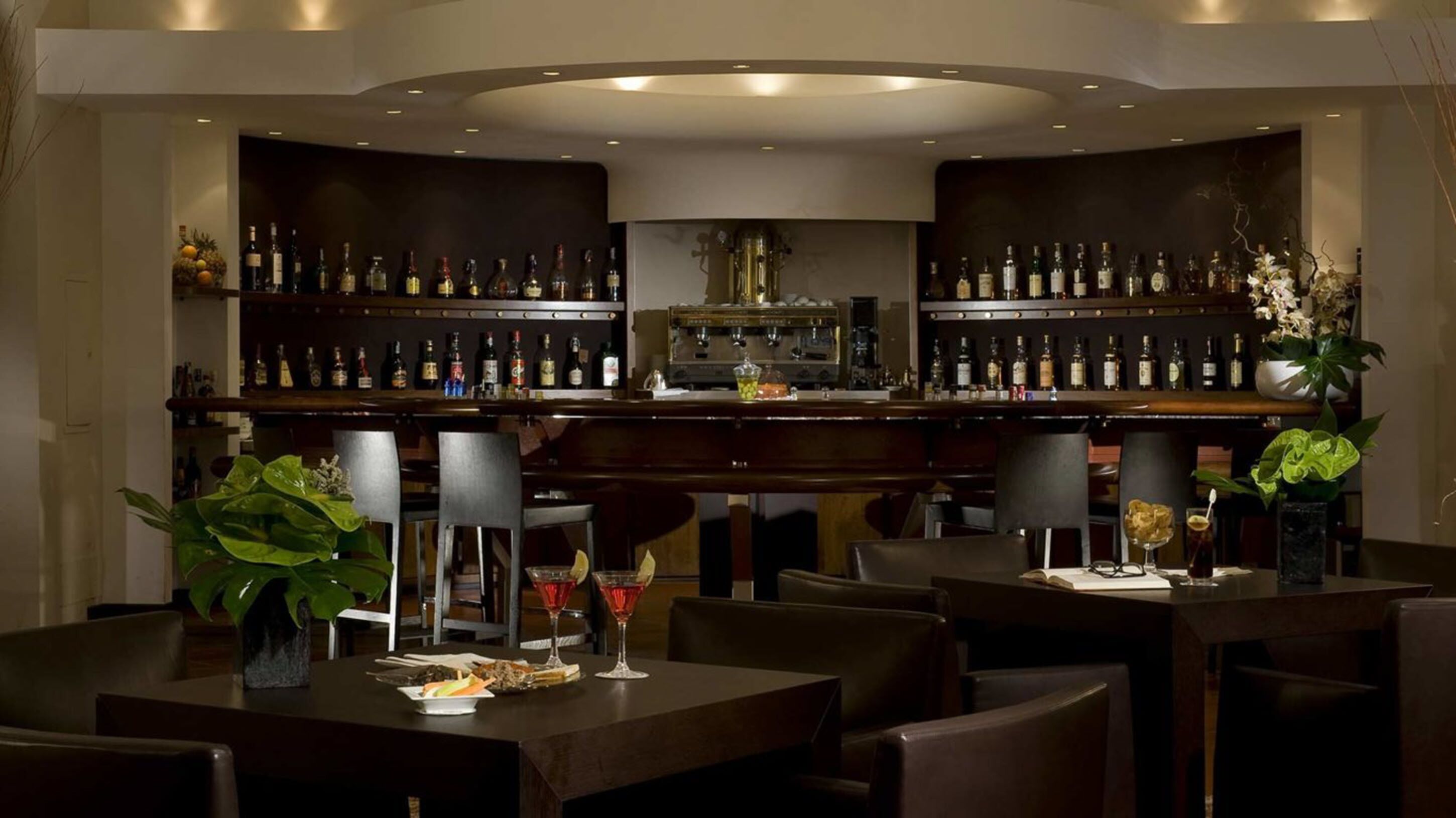 Uma área de bar com diversos assentos e uma variedade de garrafas nas prateleiras.