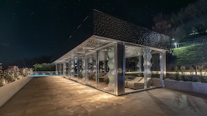 Una estructura moderna de vidrio con áreas de descanso, piscina y un cielo estrellado.