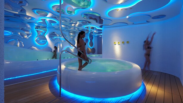 Piscina interior moderna con diseño de techo único e iluminación azul.