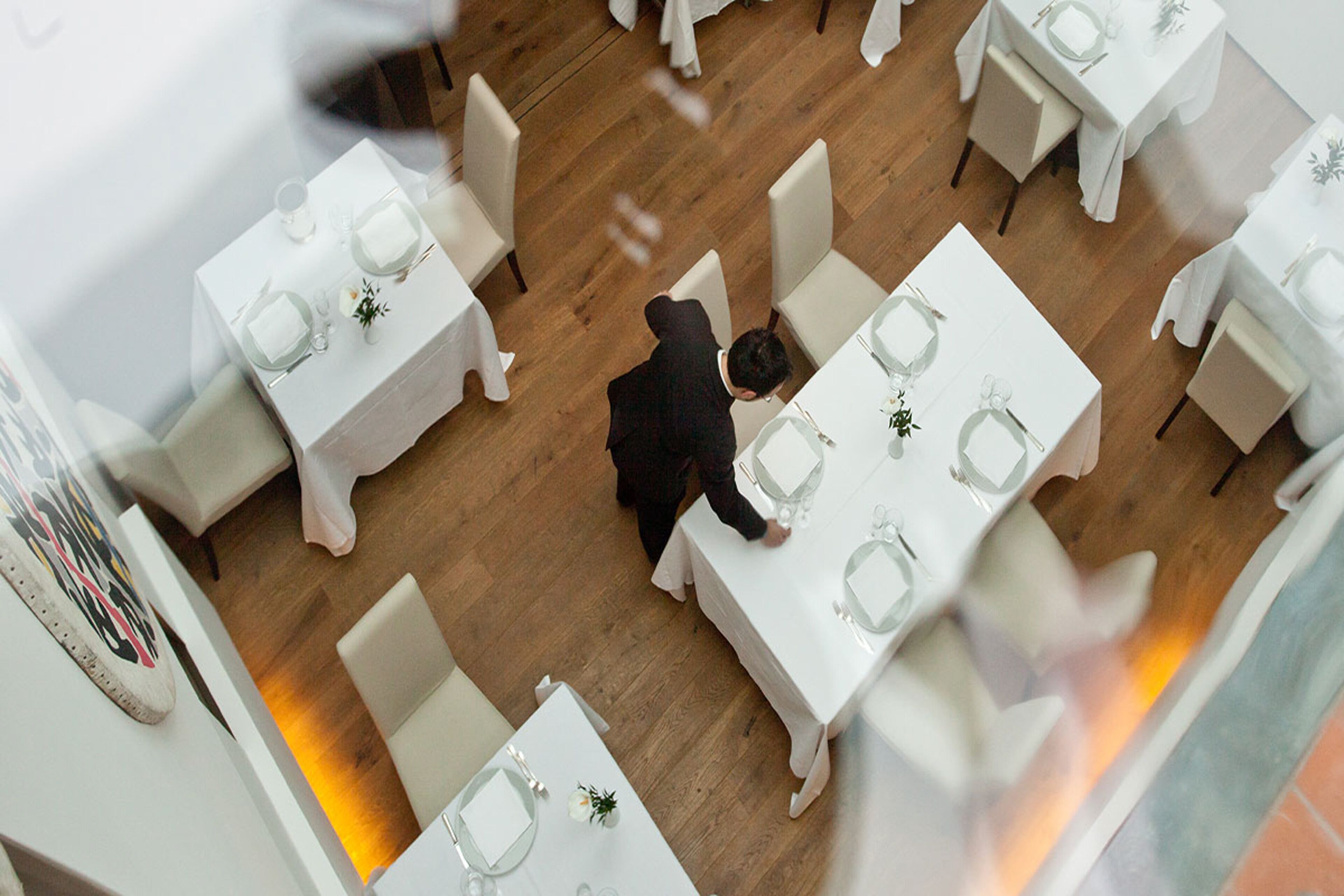 Une vue aérienne d’un restaurant avec de nombreuses tables, chacune étant dressée avec une nappe blanche et des couverts en argent.