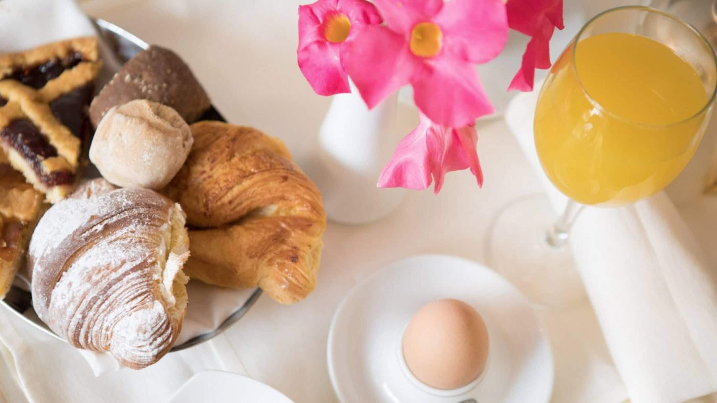 A breakfast setting with pastries, a glass of orange juice, and a flower arrangement.